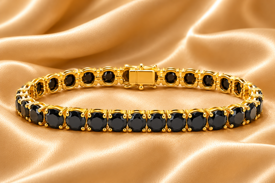 A gold tennis bracelet with round black gemstones, displayed on a draped champagne-colored satin fabric background.