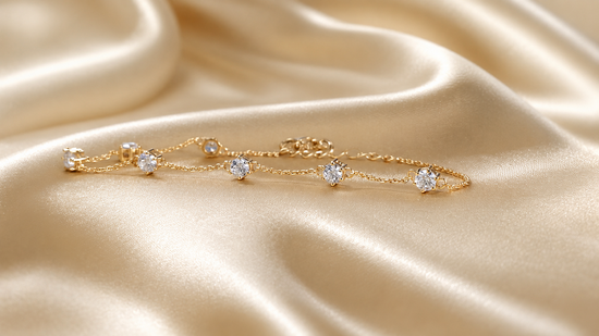 A delicate gold chain bracelet with five round clear gemstones, displayed on draped champagne-colored satin fabric.