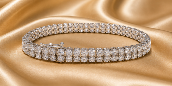 A double-row tennis bracelet paved with sparkling clear gemstones in a silver-toned setting, displayed on a draped gold satin fabric background.