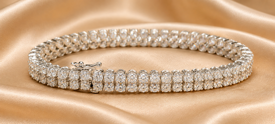 A diamond tennis bracelet with a silver-toned clasp, displayed on a draped beige satin fabric background.