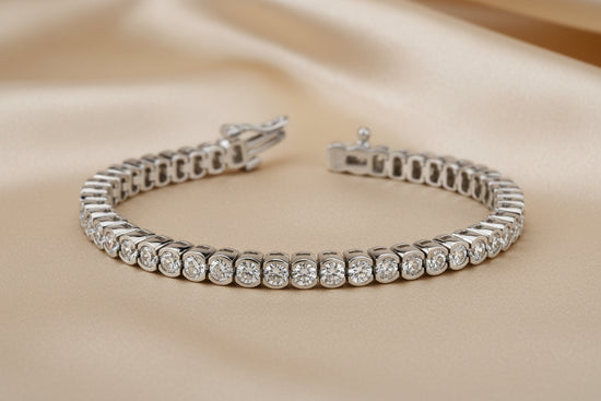 A silver tennis bracelet with round-cut clear stones, shown open on a reflective white surface.