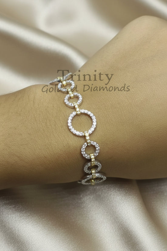 A gold and diamond link bracelet worn on a wrist, featuring a vertical arrangement of oval and spiral links set with clear stones, resting on a beige satin fabric background. A watermark for &