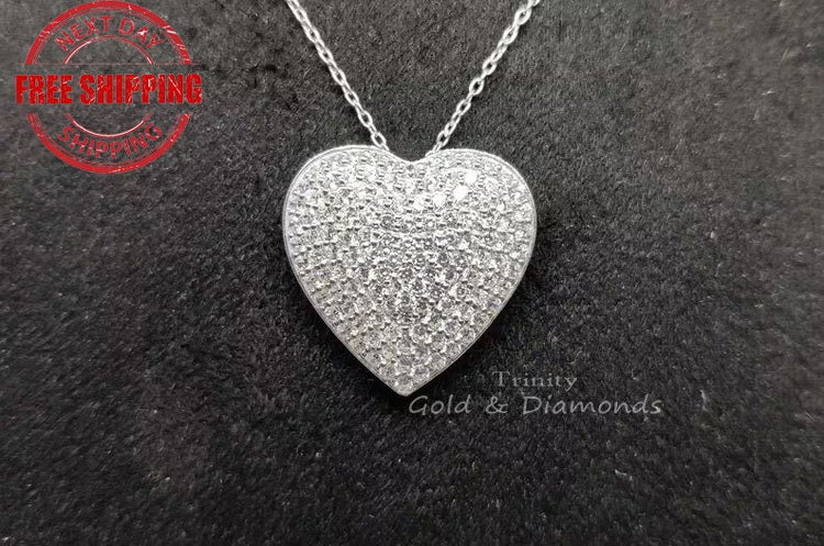 A silver heart-shaped pendant with a pave diamond pattern, displayed against a black background with a watermark/logo in the top left corner.