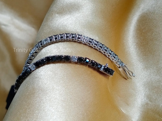A tennis bracelet featuring black and white moissanite stones set in a silver band, displayed on a yellow fabric surface.