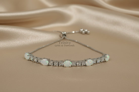 A silver tennis bracelet with round white opal and clear accent stones, displayed on a light gray surface with a matching silver clasp visible in the background.