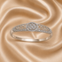 A silver filigree bangle bracelet with a central round diamond cluster and pavé-set diamonds along the band, displayed on a draped champagne satin fabric.