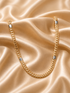A gold-toned Cuban link chain necklace with silver-toned rectangular end caps, draped on a shiny champagne satin fabric background.