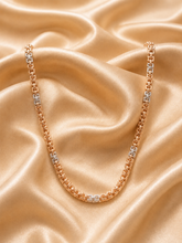 A rose gold tennis necklace with alternating clear gemstone links, draped elegantly on a draped champagne satin fabric background.