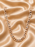 A chunky gold-toned Cuban link chain necklace with rectangular links, displayed on a draped champagne satin fabric background.