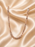 A rose gold tennis necklace with clear gemstones, draped in a U-shape over a beige satin fabric background.