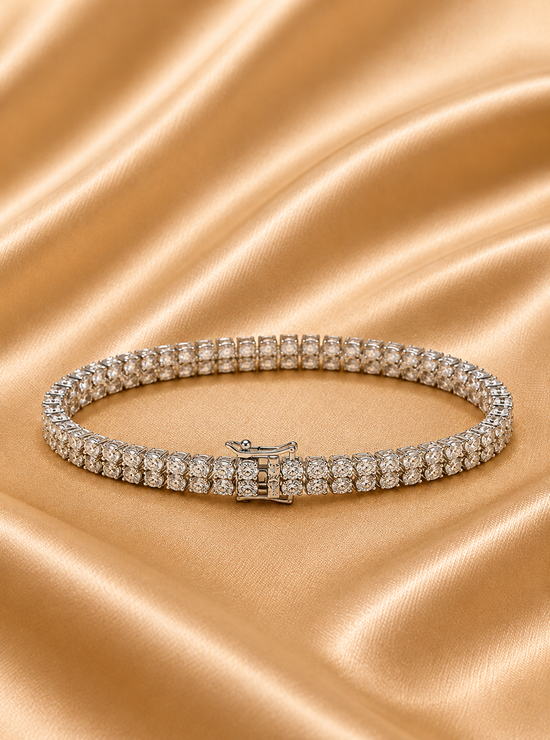 A double-row diamond tennis bracelet with a signature H-shaped clasp, displayed on a draped champagne satin fabric background.