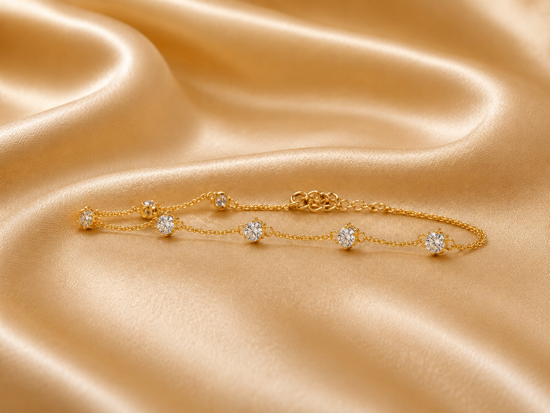 A delicate gold chain bracelet with five round-cut clear gemstones, displayed on draped champagne-colored satin fabric.