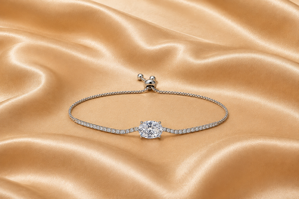 A silver-toned adjustable bracelet featuring a central round-cut clear gemstone and a pavé-set band, displayed on a draped champagne satin fabric.