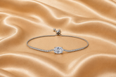 A silver-toned adjustable bracelet featuring a central round-cut clear gemstone and a pavé-set band, displayed on a draped champagne satin fabric.