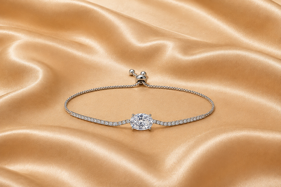 A silver-toned adjustable bracelet featuring a central round-cut clear gemstone and a pavé-set band, displayed on a draped champagne satin fabric.