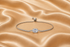 A silver-toned adjustable bracelet featuring a central round-cut clear gemstone and a pavé-set band, displayed on a draped champagne satin fabric.