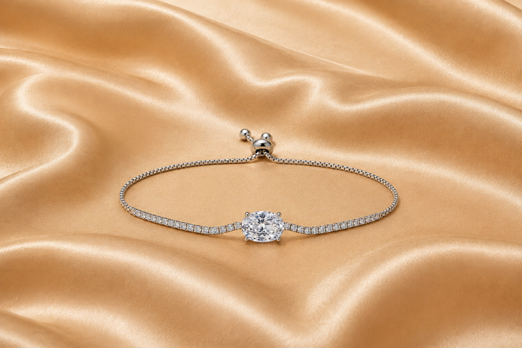 A silver-toned adjustable bracelet featuring a central round-cut clear gemstone and a pavé-set band, displayed on a draped champagne satin fabric.