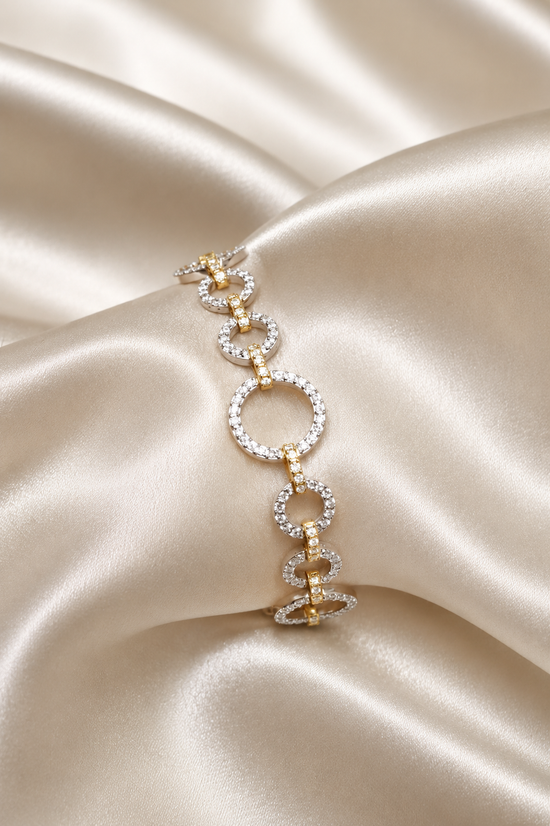 A two-tone gold and white gold bracelet with circular and spiral link designs, embellished with pavé diamonds, displayed on draped champagne satin fabric.
