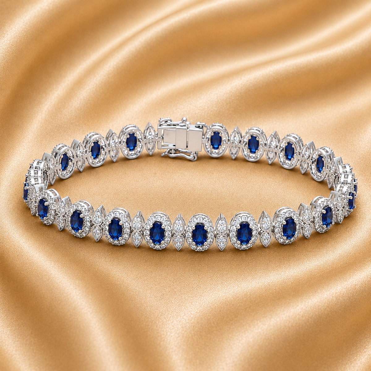 A silver tennis bracelet with oval blue gemstones and clear stones, displayed on a draped champagne satin fabric.