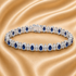 A silver tennis bracelet with oval blue gemstones and clear stones, displayed on a draped champagne satin fabric.