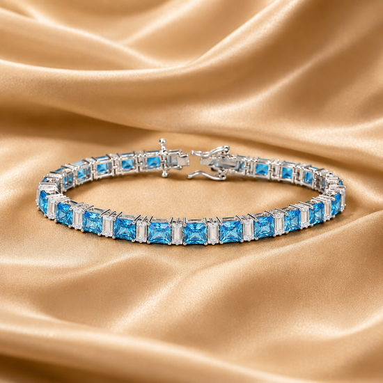 A silver tennis bracelet featuring rectangular blue gemstones, displayed on a draped beige satin fabric background.