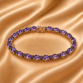 A close-up of a bracelet laid diagonally across draped champagne satin fabric. The bracelet features round purple gemstones in a silver-toned setting.