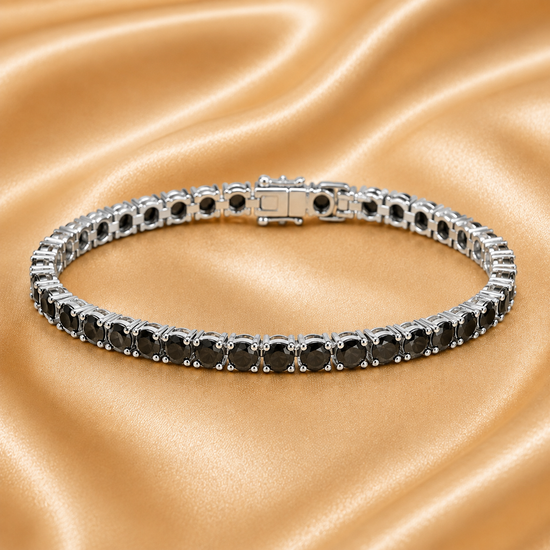 A single tennis bracelet with round black gemstones in a silver-toned setting, displayed on a beige satin fabric background. A faint &