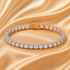 A curved tennis bracelet with baguette-cut clear stones in a silver-toned setting, displayed on draped champagne satin fabric.