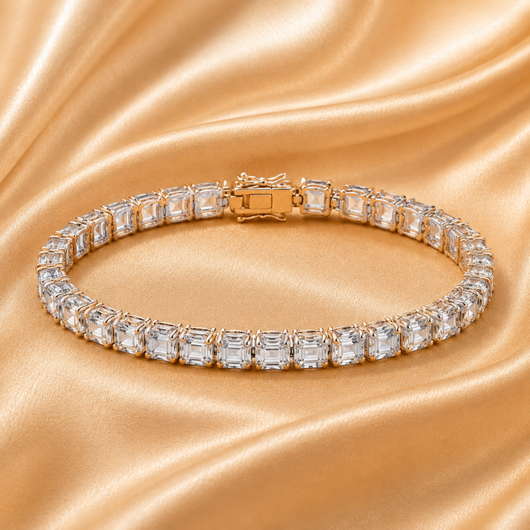 A curved tennis bracelet with baguette-cut clear stones in a silver-toned setting, displayed on draped champagne satin fabric.
