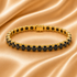 A gold tennis bracelet with round black gemstones, displayed on a draped champagne-colored satin fabric background.
