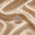 A silver peace sign pendant necklace encrusted with small clear stones, held in the palm of a hand against a draped champagne satin fabric background.