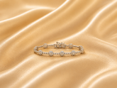 Delicate diamond tennis bracelet with floral cluster detailing arranged on luxurious golden silk fabric.