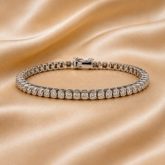A silver tennis bracelet with round-cut clear stones, displayed on a draped champagne satin fabric background.