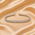 A tennis bracelet with clear gemstones in a silver-toned setting, displayed on a draped champagne satin fabric background.
