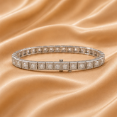 A diamond tennis bracelet in a silver-toned setting, displayed on a draped champagne satin fabric background.