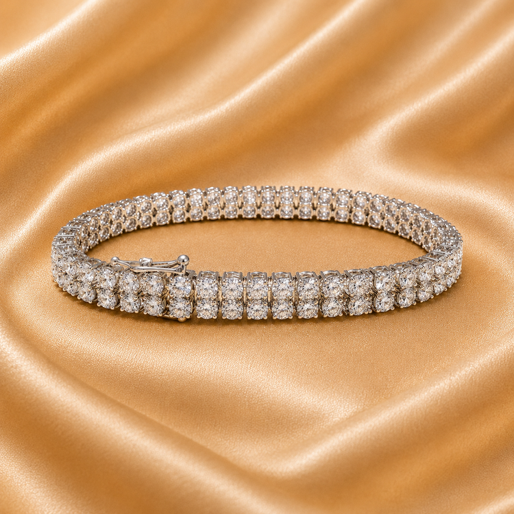 A double-row diamond tennis bracelet in a silver-toned setting, displayed on a draped champagne-gold satin fabric background.