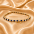 A gold tennis bracelet adorned with round blue sapphires and clear cubic zirconia stones, displayed on a draped champagne satin fabric.