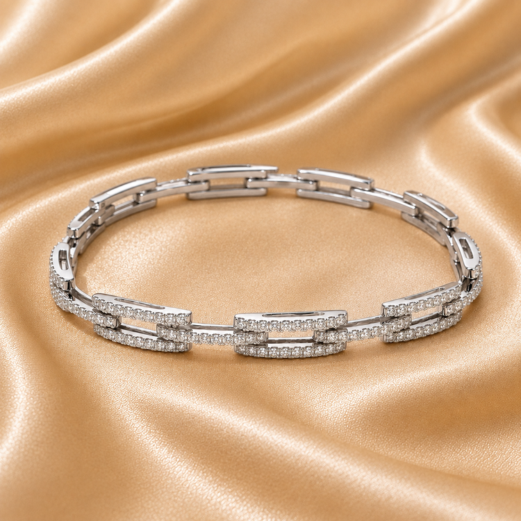 A silver-toned link bracelet with rectangular links paved with small clear stones, displayed on a draped champagne satin fabric background.