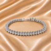 A sparkling diamond tennis bracelet with a silver-toned clasp, displayed on draped champagne satin fabric.