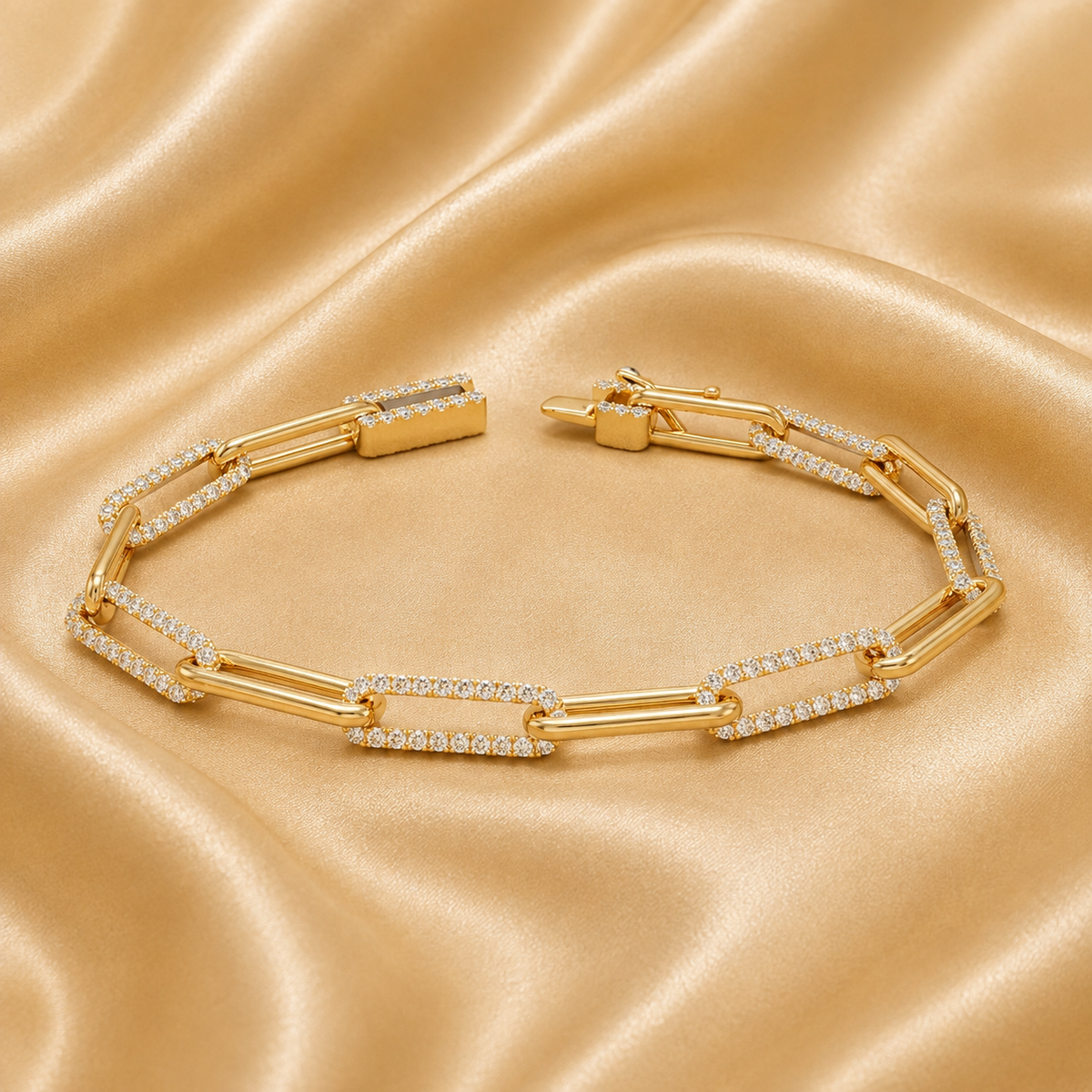 A gold link bracelet with pavé-set clear stones, arranged in an oval shape on a draped champagne satin fabric background.