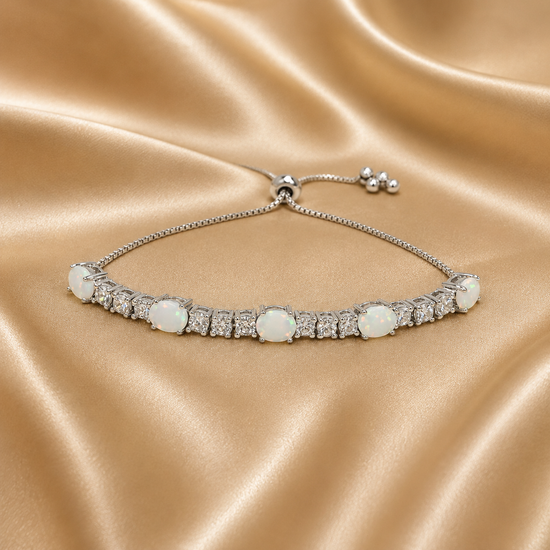 A silver tennis bracelet with round white opal and clear accent stones, displayed on a light gray surface with a matching silver clasp visible in the background.