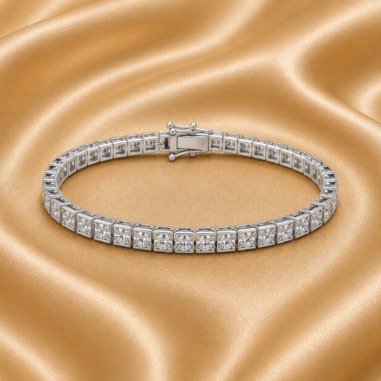 A silver tennis bracelet with square-cut clear stones, displayed on a draped gold satin fabric background.