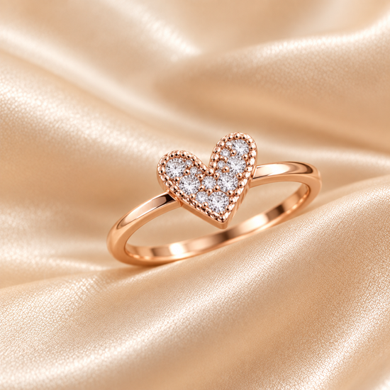 A close-up of a rose gold ring with a heart-shaped pavé setting worn on a finger, set against a soft beige satin fabric background.