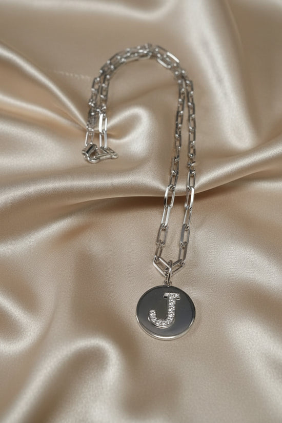 A silver chain necklace with a round silver pendant engraved with the letter &
