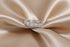 A silver band ring with baguette-cut clear stones, displayed on a draped champagne-colored satin fabric.
