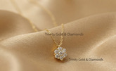 A gold flower-shaped pendant necklace with clear stones, resting on draped champagne-colored satin fabric. The brand name &