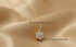 A gold flower-shaped pendant necklace with clear stones, resting on draped champagne-colored satin fabric. The brand name &