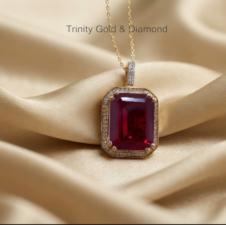 A rectangular emerald-cut red gemstone pendant necklace in yellow gold with a diamond halo, resting on draped champagne-colored satin fabric. The text &