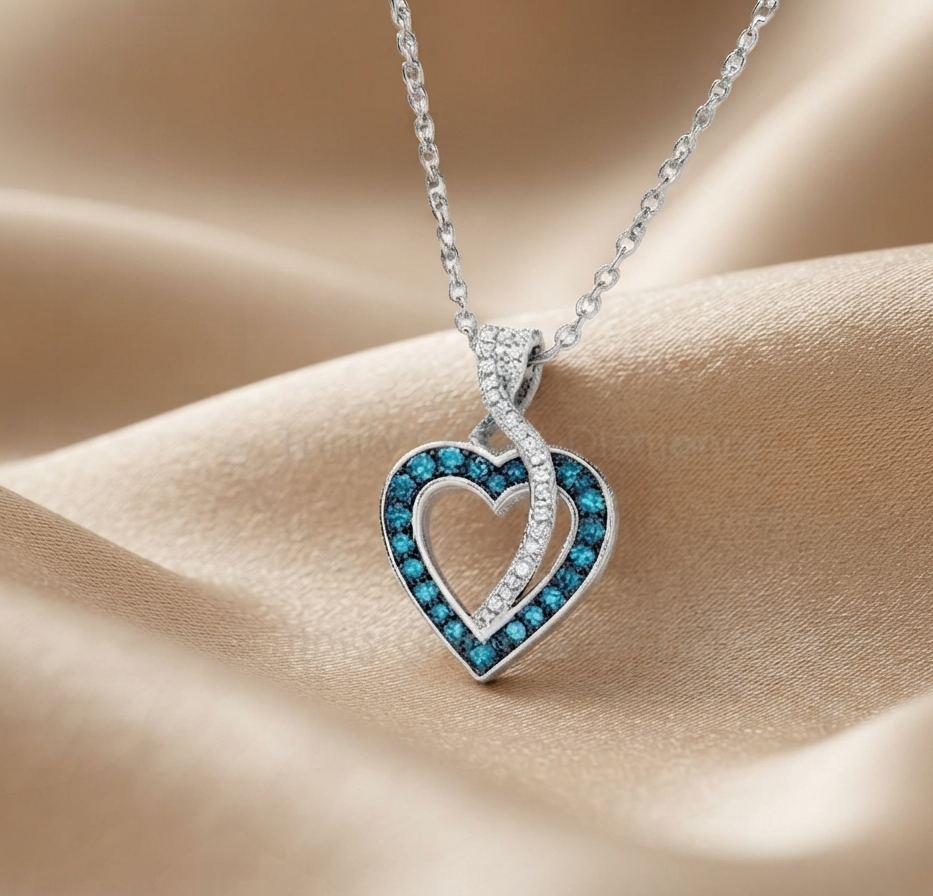 A silver heart-shaped pendant necklace with a vibrant blue gemstone border, resting on draped beige satin fabric.