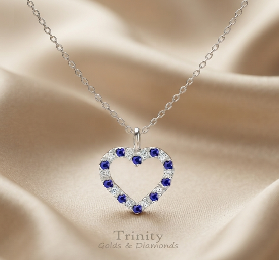 A silver heart-shaped pendant necklace with blue gemstones, displayed on a beige satin fabric background. The brand name &